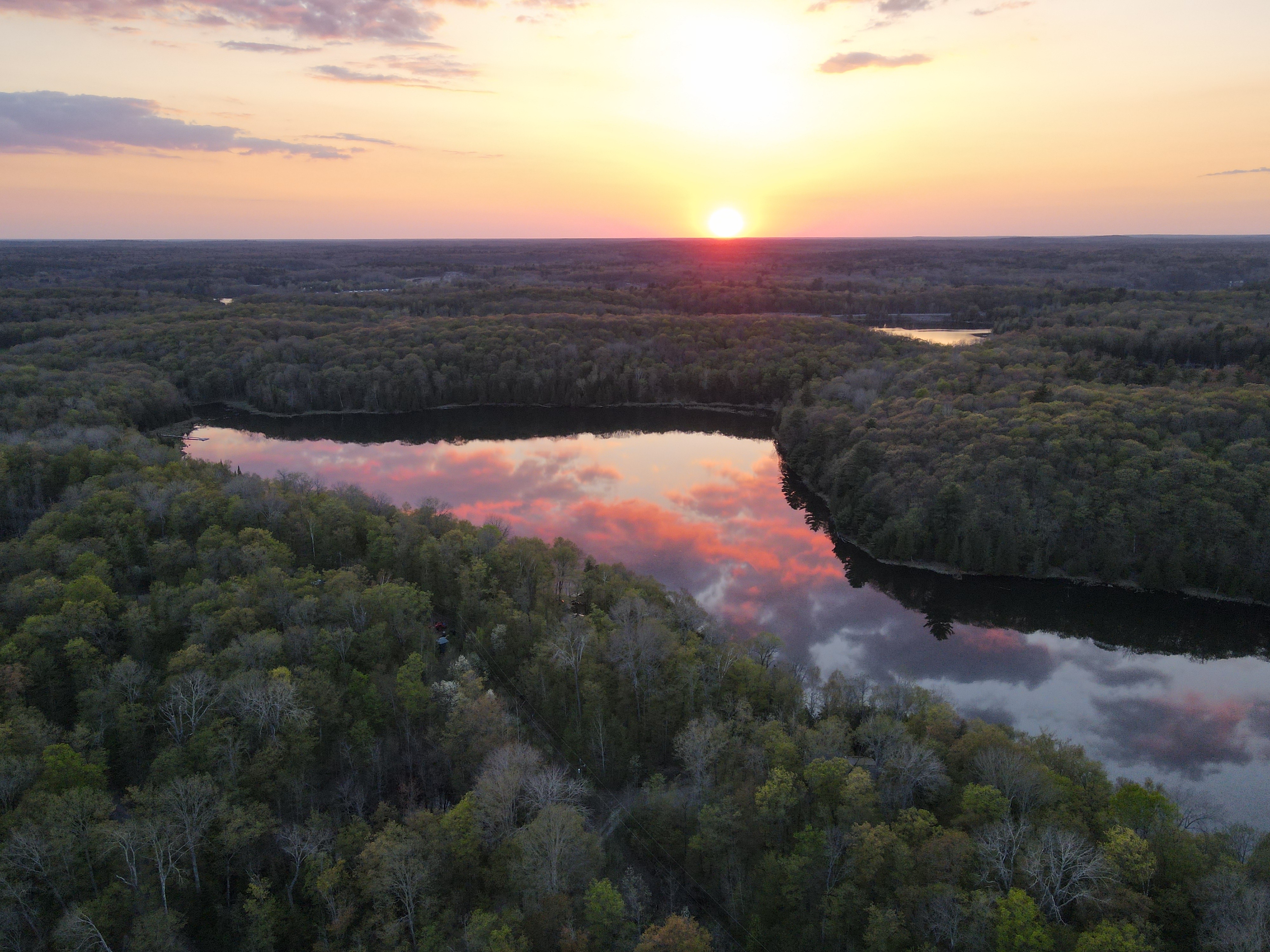 Arial photo at sunset of the lake the property sits on, the calm lake reflecting the purple, pink, and orange sky.