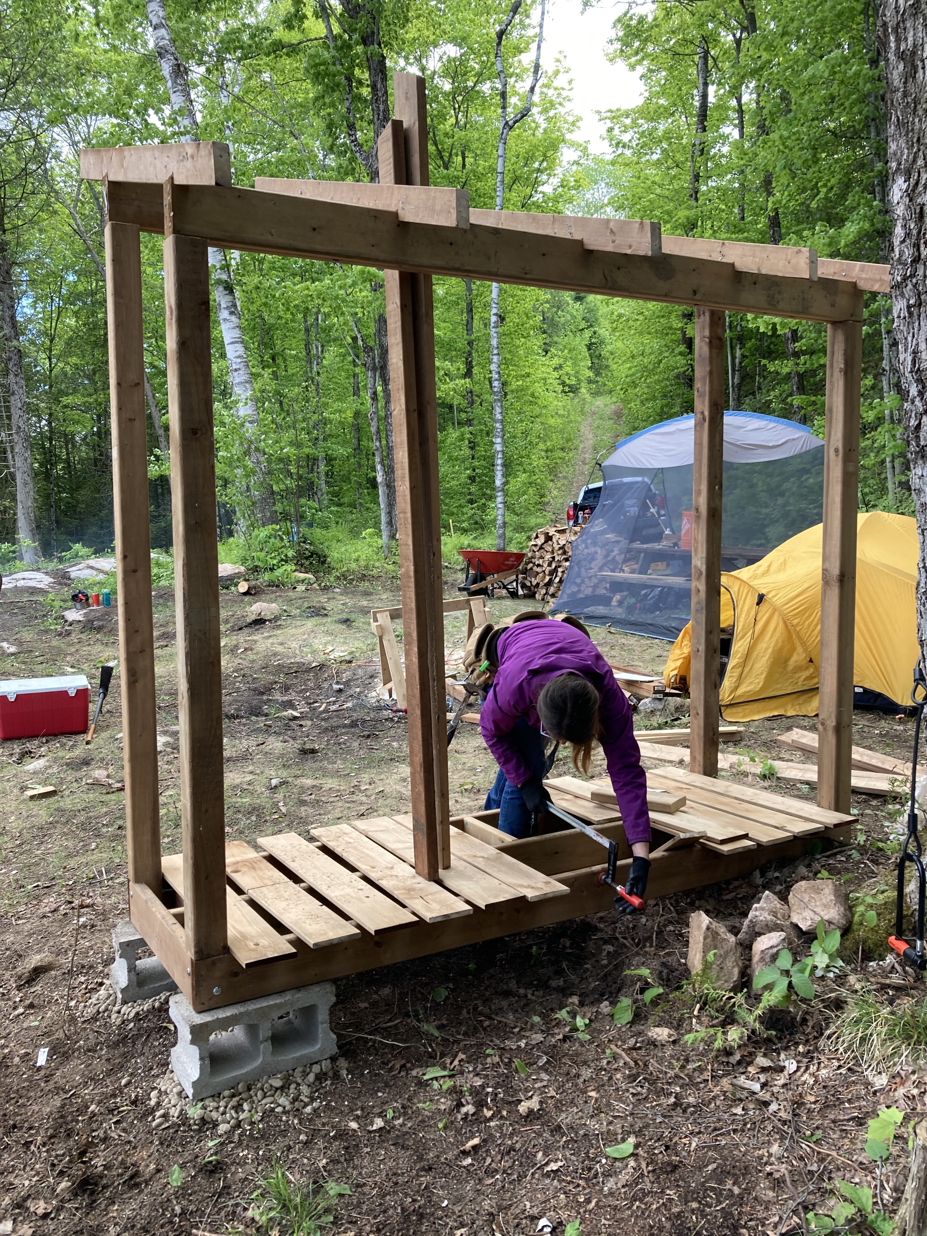 The firewood storage shed in construction. It is 8 feet wide, 3 feet deep, and about 7 feet tall and has a single-pitch roof. It is divided into two halves and is completely open to the air.