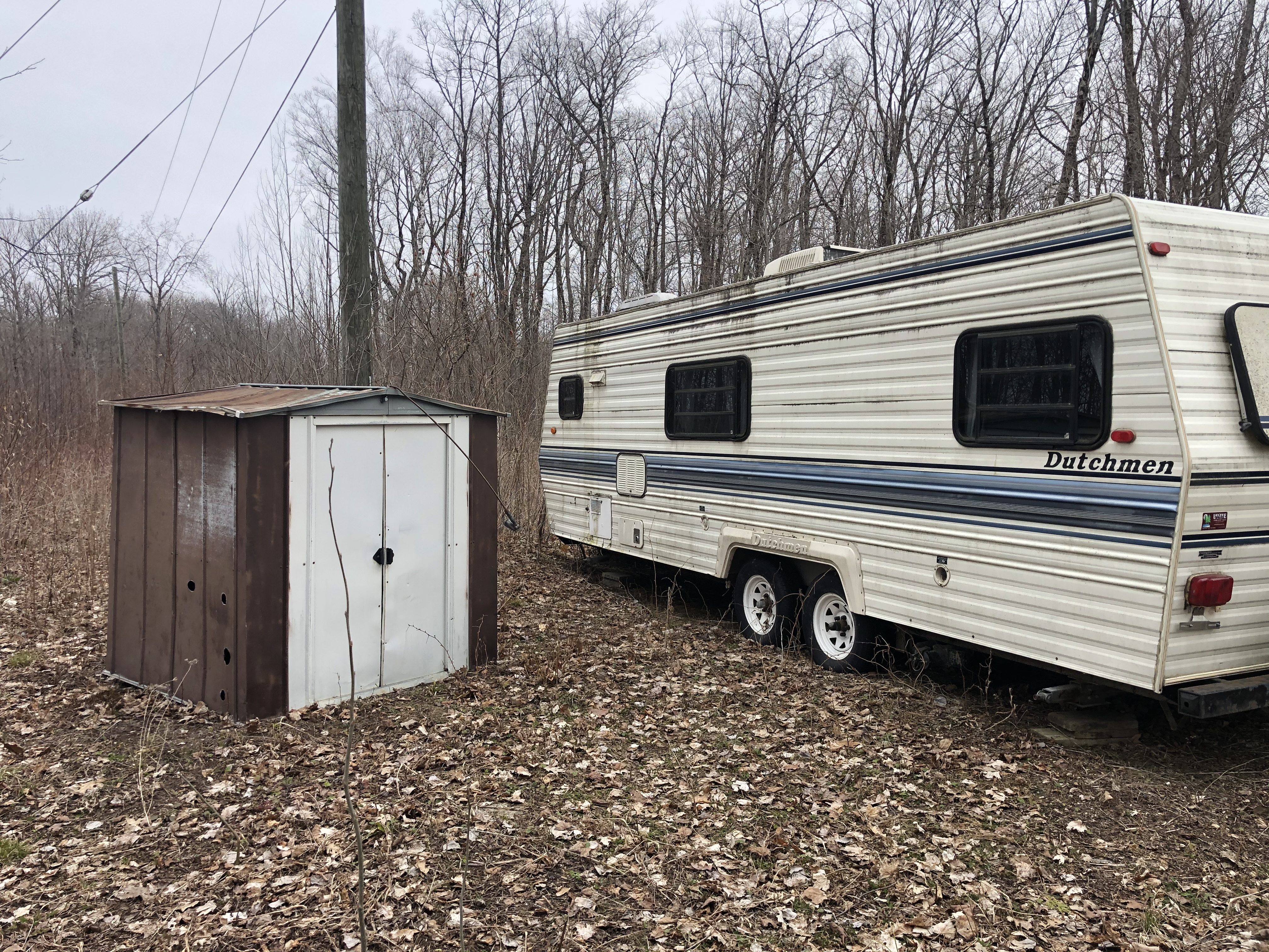 A disheveled camper trailer next to a steel garden shed