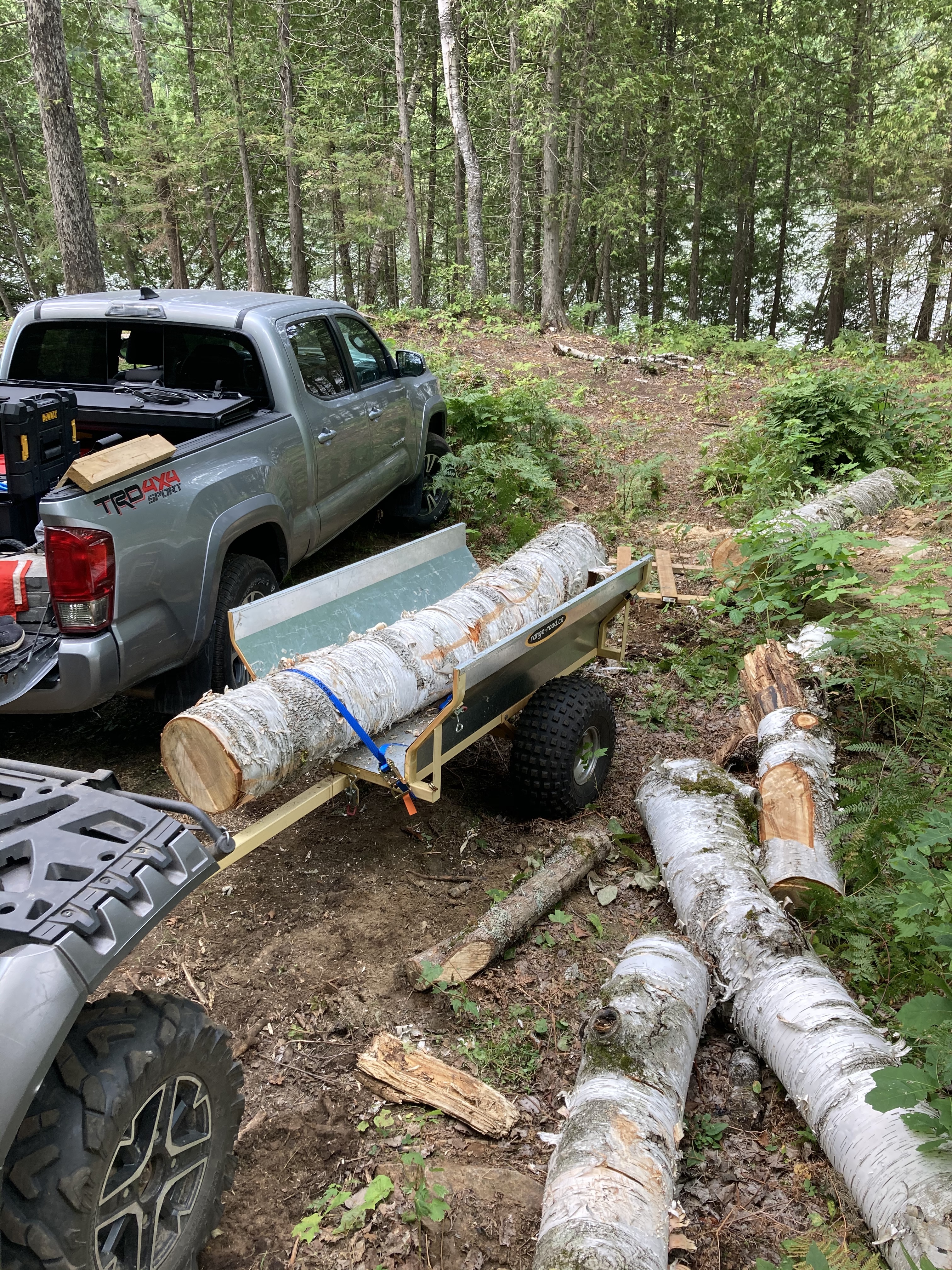 The ATV trailer with the front and rear panels missing, and an eight foot long white birch log strapped down in it