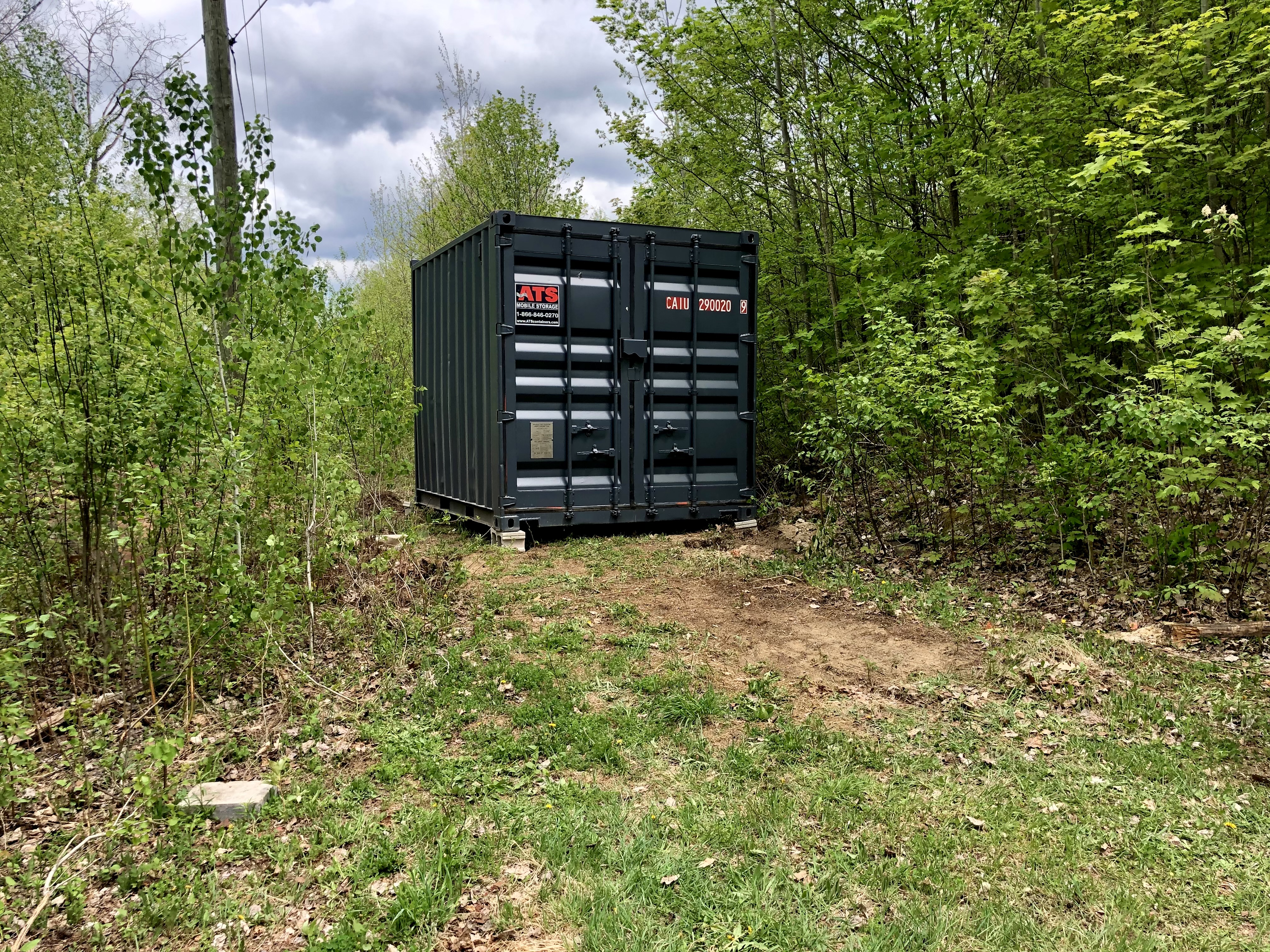 A small (ten foot), grey shipping container plopped down in the grass