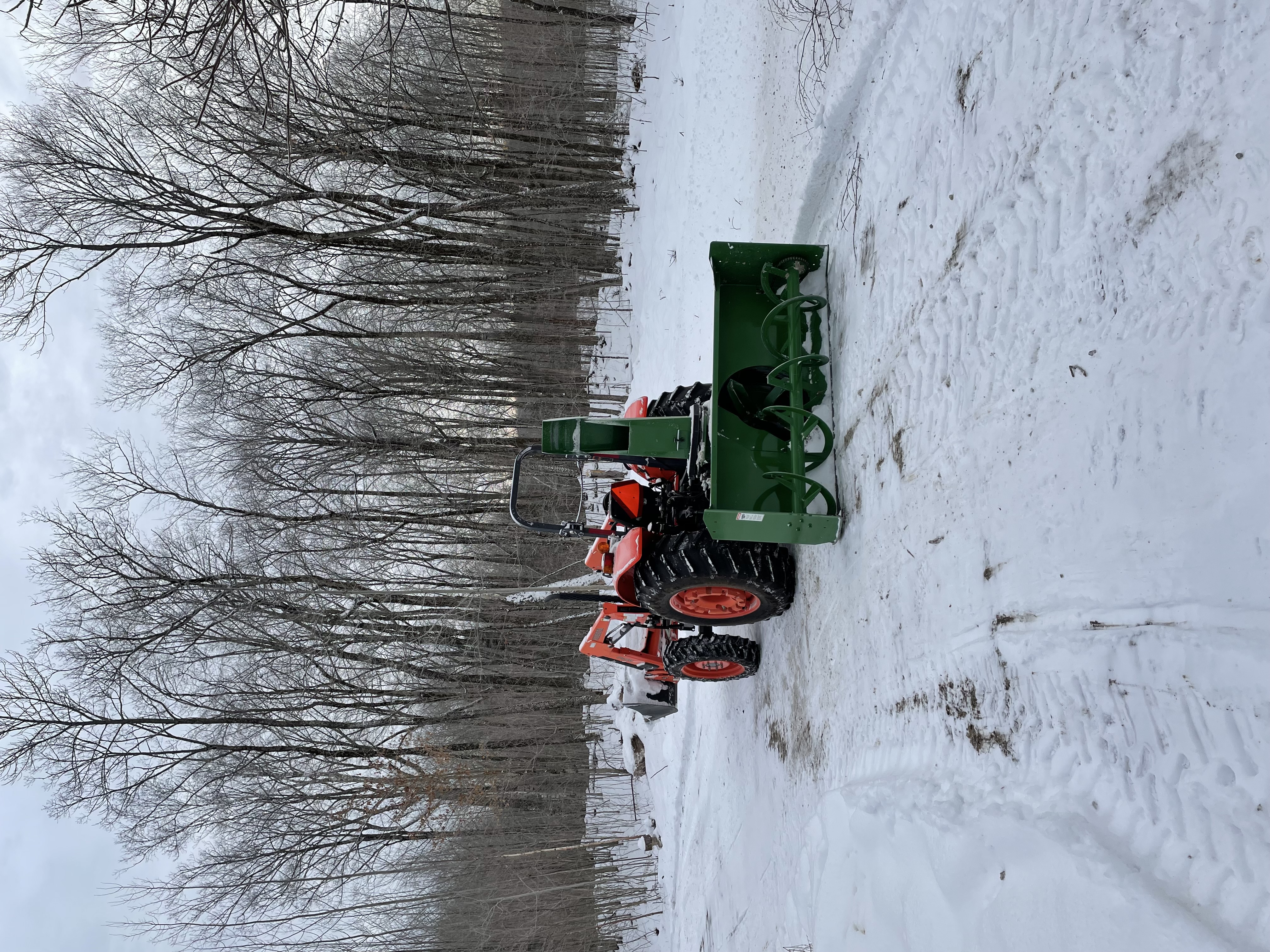 Rear view of the snow blower attached to the tractor, on a slightly snowy driveway