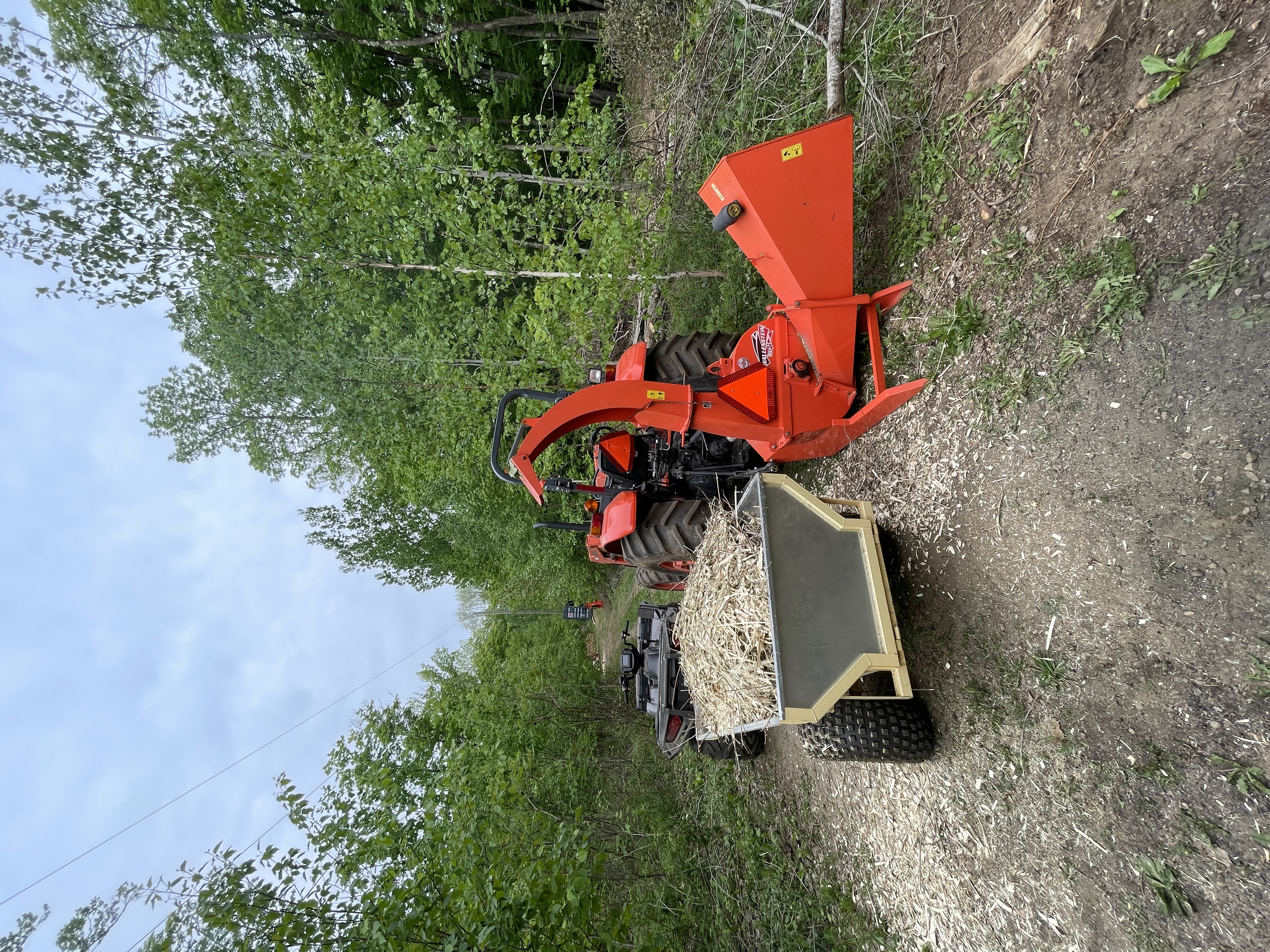 The wood chipper attached to the tractor, beside the ATV and its trailer, full of chips