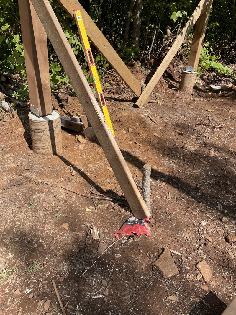 A footing with its saddle installed in concrete, and a 6x6 post set in the saddle. A brace is holding the post upright.