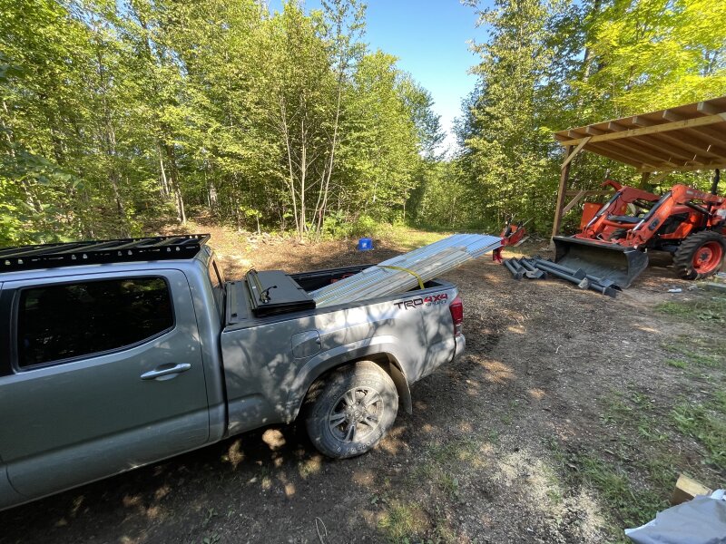 The Tacoma, backed up to the shed complete except for the roof, a pile of steel columns on the ground in front of the tractor, which is in the shed