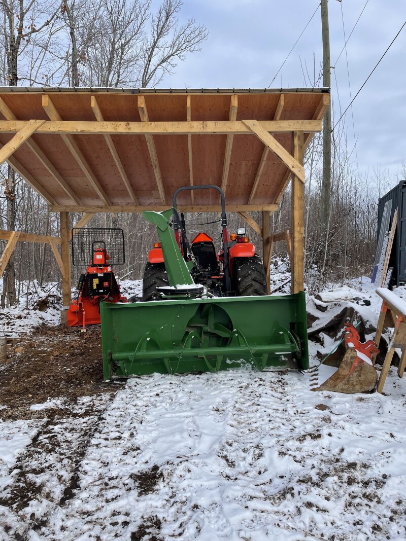 The tractor parked with the snow blower attached, in the tractor shed