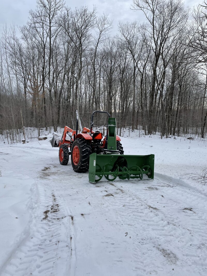 Rear view of the snow blower attached to the tractor, on a slightly snowy driveway