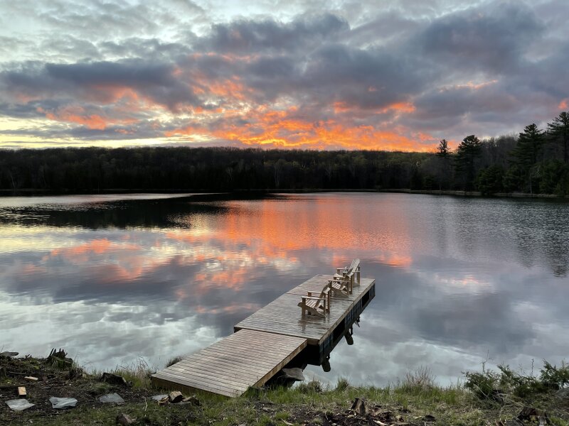 The finished dock, complete with Muskoka chairs, floating in calm water in front of a sunset