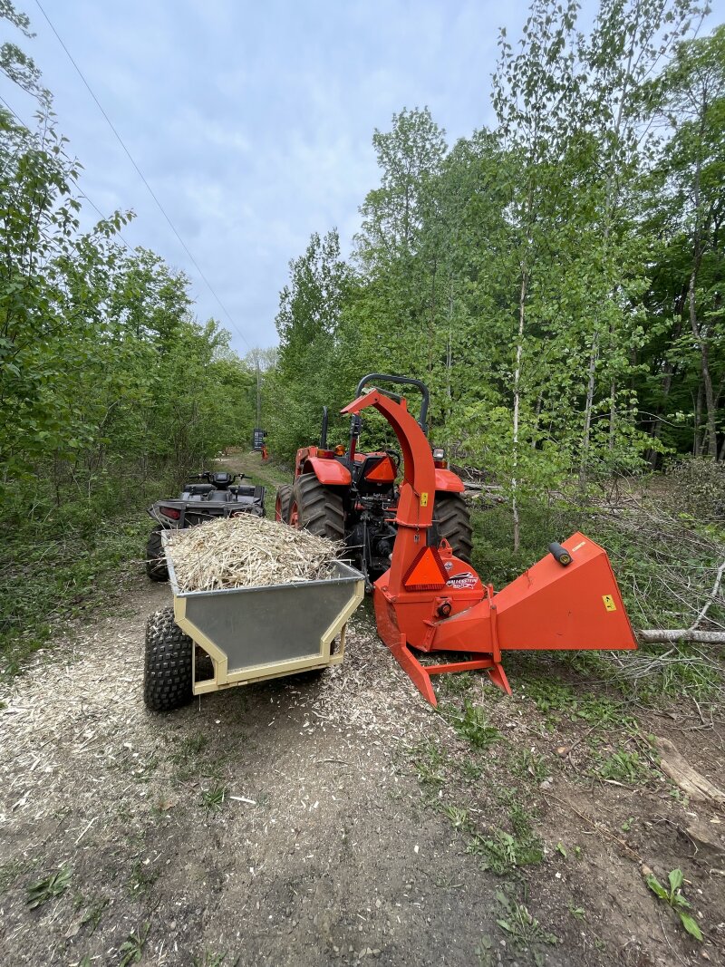 The wood chipper attached to the tractor, beside the ATV and its trailer, full of chips