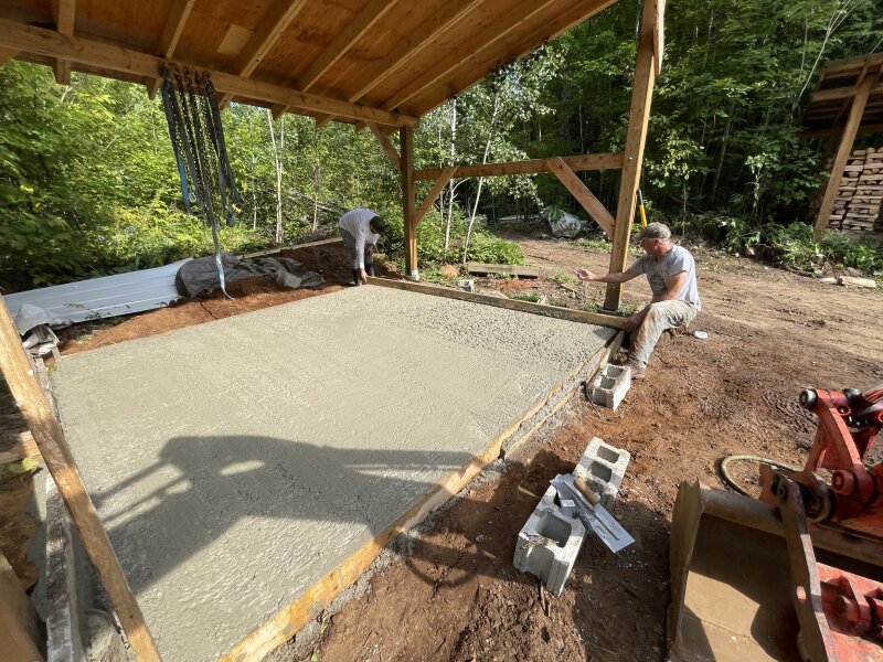 Fresh concrete being spread out by two friends with a makeshift “screed bar,” a long 2 x 4 riding on either side of the form