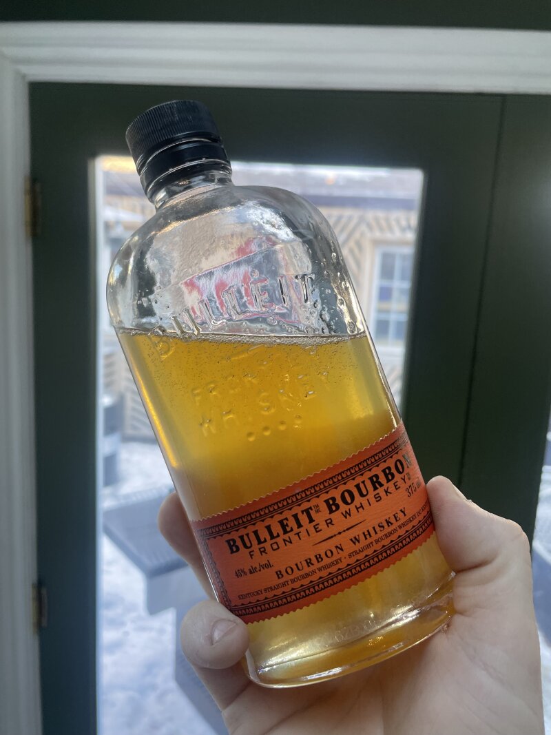A Bulleit Bourbon bottle about 3/4 full of slightly cloudy, light golden syrup