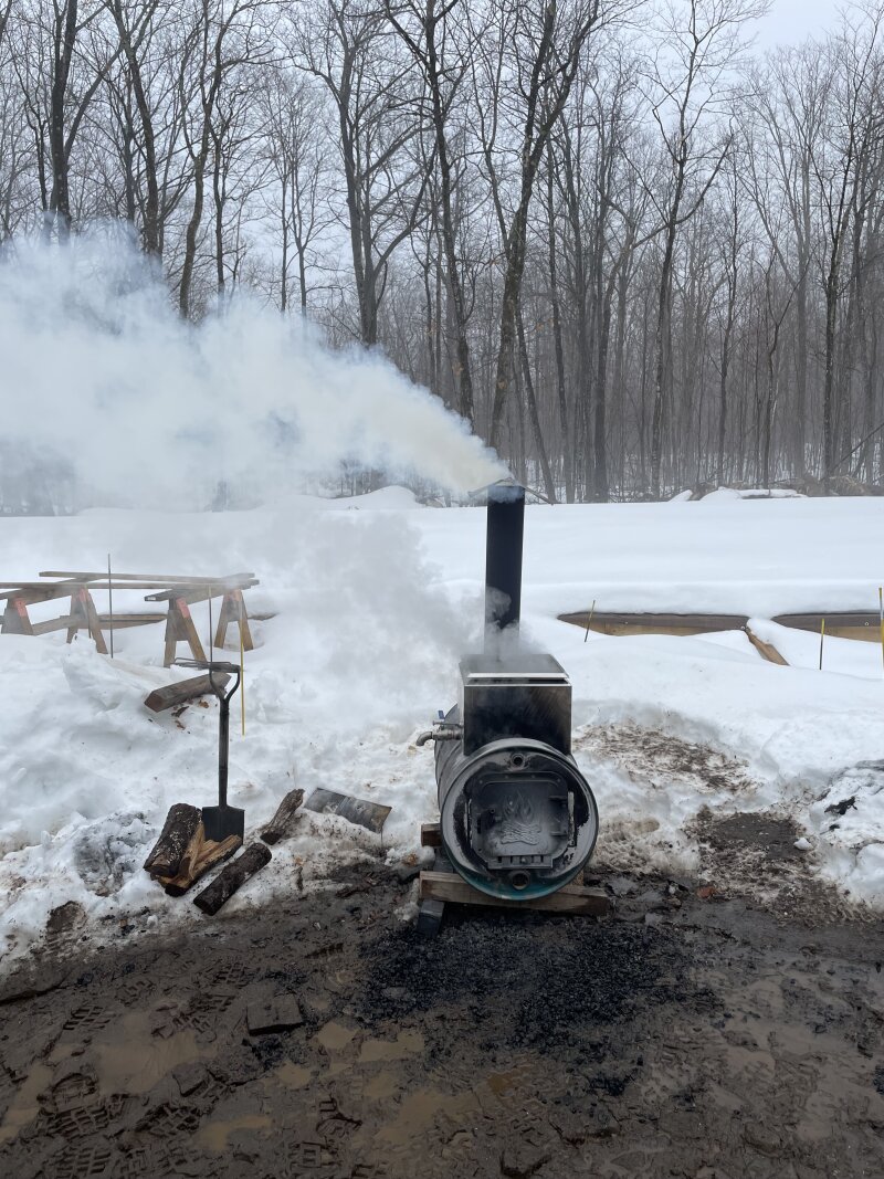 The barrel evaporator up to temperature on a cloudy day, smoke coming from the chimney and steam from the pan