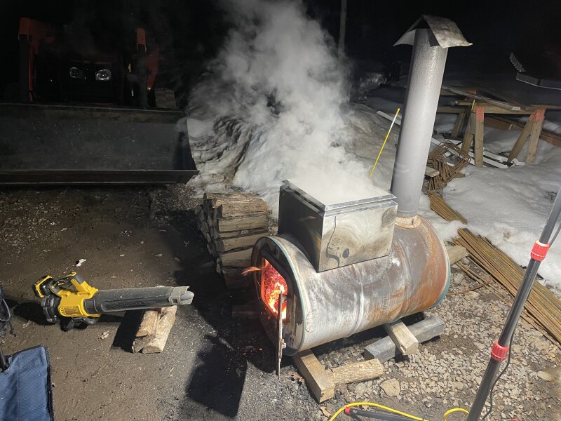 The barrel evaporator boiling away during a dark evening, an electric leaf blower forcing air into its open door